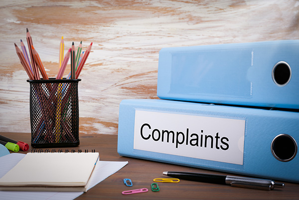 Image shows a stack of files on a table with some pencils in a pot and a small note pad. One the lower file the words read "Complaints"